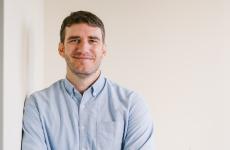 Man smiling and leaning up against a wall while wearing a dress shirt