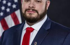 Man with a beard wearing a suit with a red tie looking at the camera