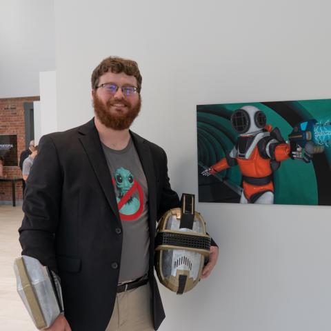 Faculty member poses next to his artwork on display