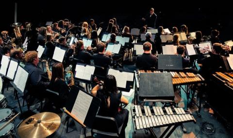 orchestra members playing instruments looking at their conductor