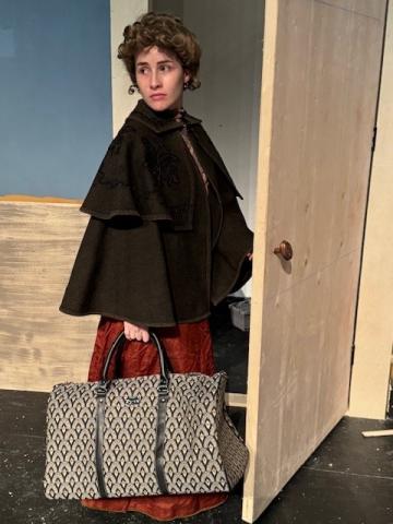 Theatre student opens a door holding a purse while rehearsing on stage