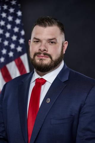 Man with a beard wearing a suit with a red tie looking at the camera